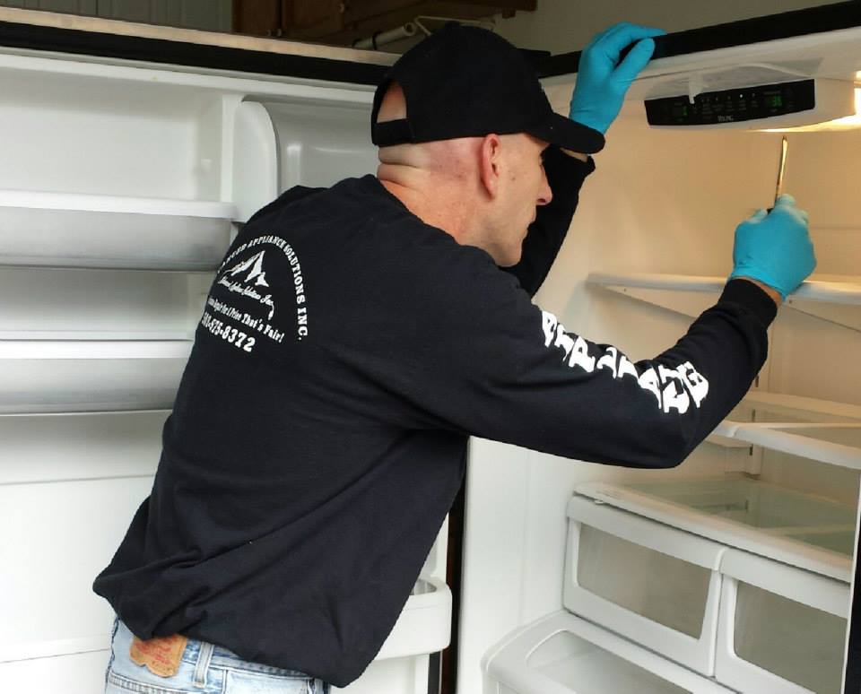 A technician in an Advanced Appliance Solutions shirt repairing a refrigerator