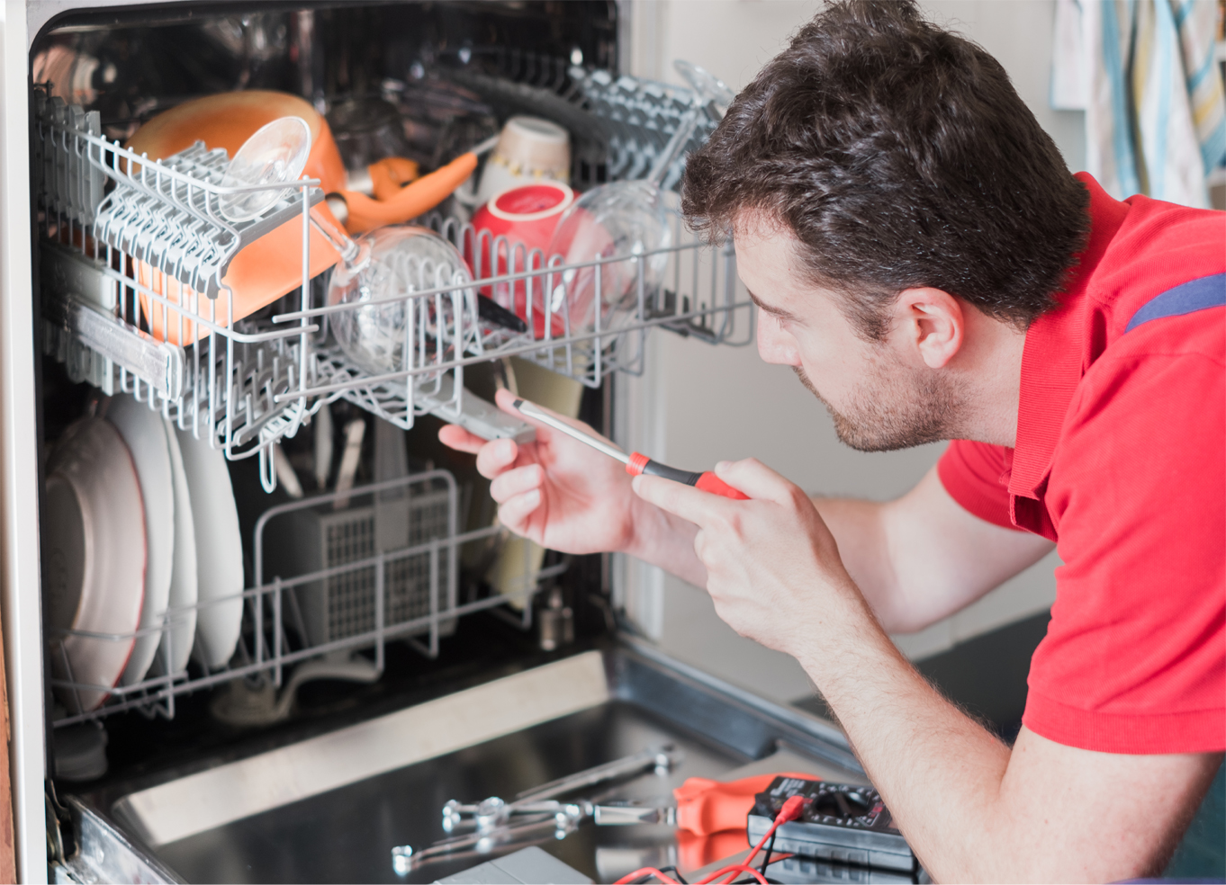 A technician in a red shirt repairing a dishwasher